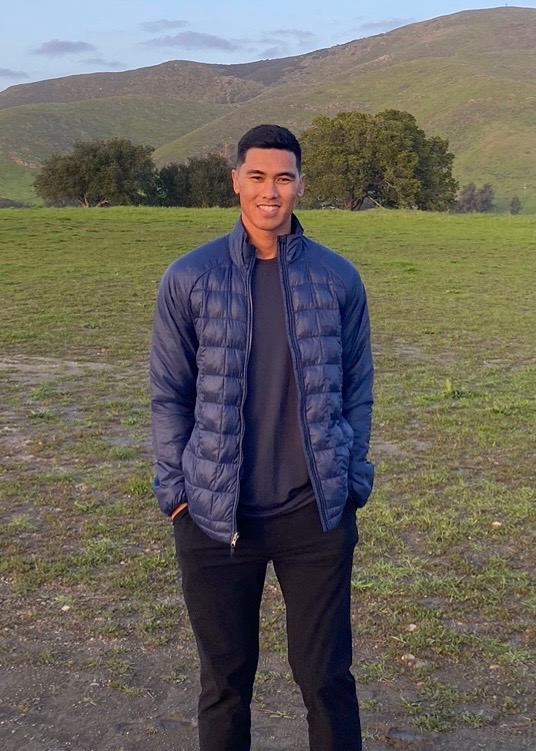 a man standing in a field with a mountain in the background