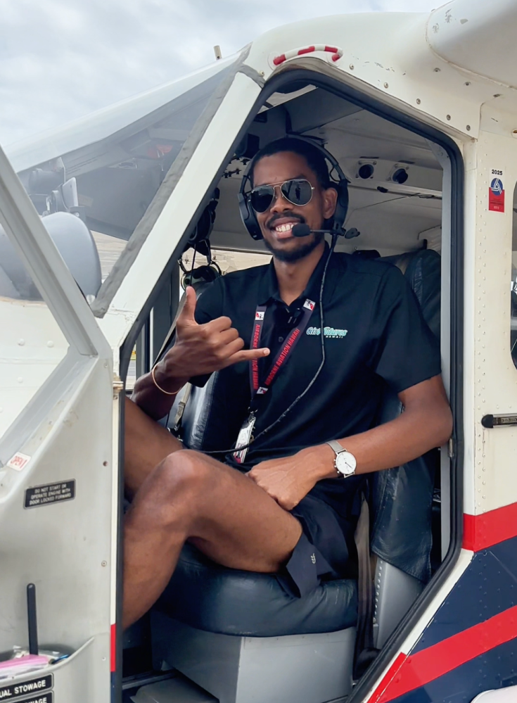 Person sitting in a small plane cockpit, wearing sunglasses and headphones, giving a thumbs-up.